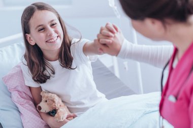 Smiling girl with plush toy giving a high five to a nurse in the hospital clipart