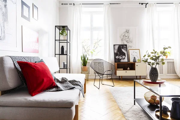 Almohada roja y manta en el sofá en el interior del loft brillante con flores en la mesa y el sillón. Foto real — Foto de Stock