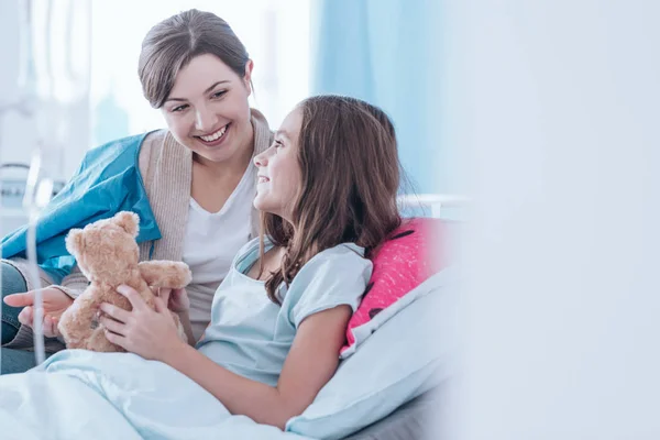 Sisters smiling and sitting together in bed in the hospital — Stock Photo, Image