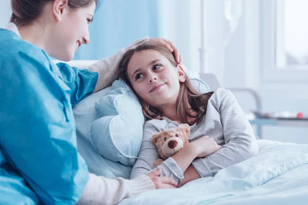 Cuidador sonriente visitando a una niña feliz y enferma en el centro de salud —  Fotos de Stock