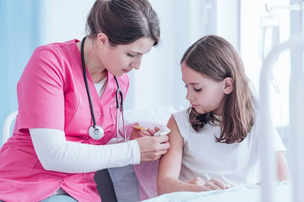 Sjuk sköterska i rosa uniform ger en injektion till en flicka på sjukhus — Stockfoto