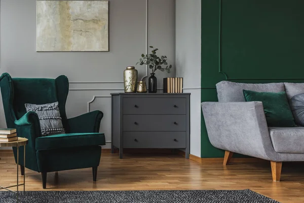 Poltrona verde esmeralda com travesseiro ao lado de commode de madeira cinza no interior da sala de estar escura — Fotografia de Stock