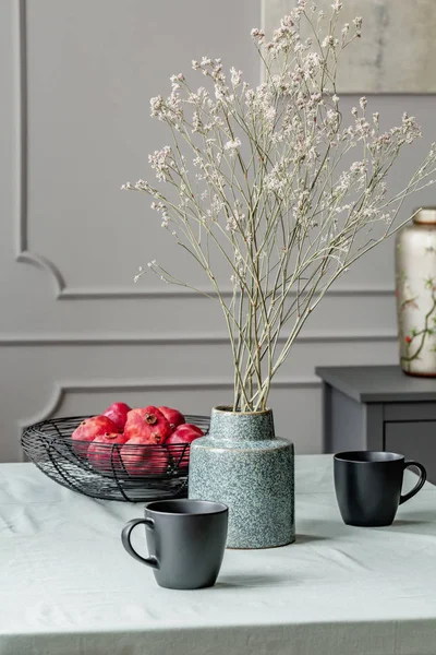 Mesa da sala de jantar com frutas na tigela, flores em vaso e canecas de café — Fotografia de Stock