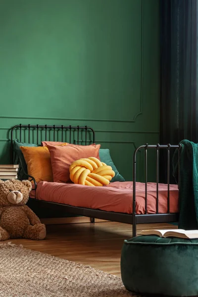 在带有深橙色床上用品的单一金属床上的黄色枕头, 在空的深绿色墙上复制空间 — 图库照片