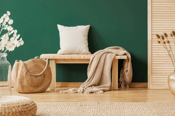 Banc en bois avec tapis beige et oreiller à côté du sac à main en paille, espace de copie sur le mur vert vide — Photo