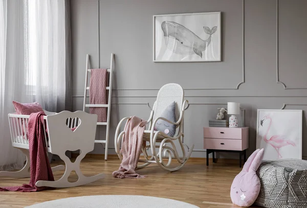 White cradle next to rocking chair in grey baby\'s bedroom interior with whale poster. Real photo