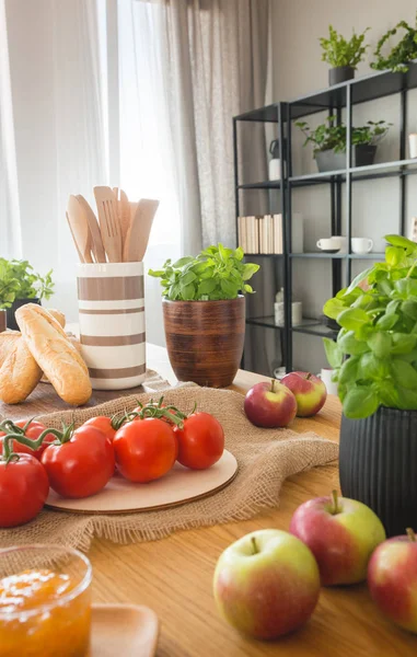 El primer plano de las manzanas, los tomates, la confitura y la albahaca sobre la mesa de comedor en el interior de la cocina — Foto de Stock