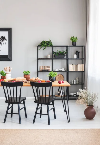 Sillas negras en mesa de madera en el interior del comedor gris con flores y alfombra marrón. Foto real — Foto de Stock