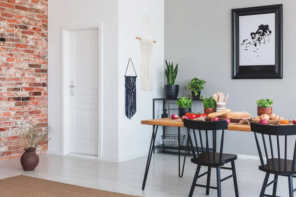 Foto reale di un moderno interno sala da pranzo con un tavolo con cibo, sedie nere e muro di mattoni — Foto Stock