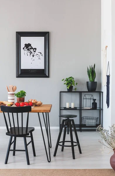 Silla negra y taburete en mesa de madera en el interior del comedor gris con plantas y póster. Foto real —  Fotos de Stock