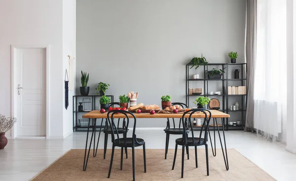 Sillas negras en mesa de madera con comida en el interior del comedor gris con puerta blanca. Foto real — Foto de Stock