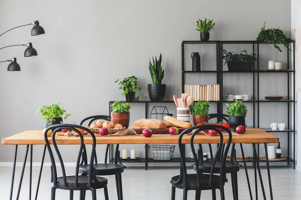 Ξύλινο τραπέζι με υγιεινά τρόφιμα στο εσωτερικό των γκρι τραπεζαρία με μαύρες καρέκλες και τα φυτά. Πραγματική φωτογραφία — Φωτογραφία Αρχείου