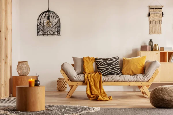 Σκανδιναβικός καναπές με μαξιλάρια και σκούρο κίτρινο κουβέρτα στο φωτεινό εσωτερικό σαλόνι με μαύρο πολυέλαιο — Φωτογραφία Αρχείου