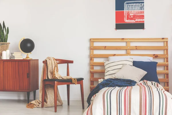 Foto real de un interior de la habitación adolescente con una cama, almohadas, una silla de madera y un póster —  Fotos de Stock