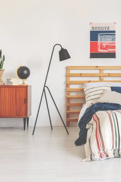 Real photo of a modern lamp in a retro bedroom interior with a bed, poster and wooden cupboard — Stock Photo, Image