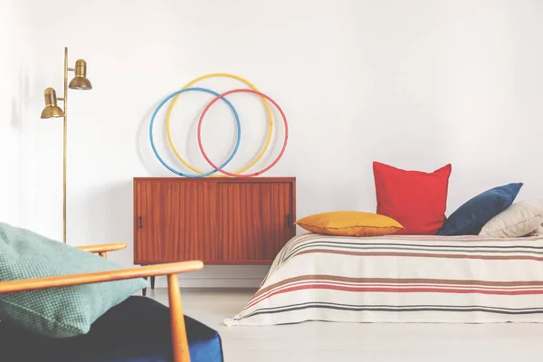 Hula hoepels op een kast naast een bed met kleurrijke kussens in een retro slaapkamer interieur — Stockfoto