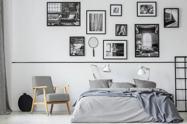 Élégant fauteuil rétro à côté du lit king size avec literie grise dans l'intérieur de la chambre contemporaine avec des photos en noir et blanc — Photo