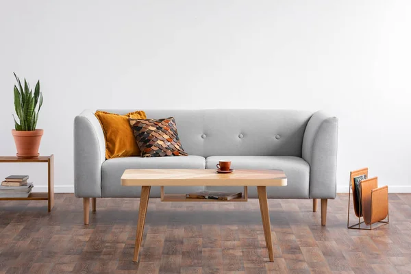 Tavolino in legno al centro di un elegante soggiorno con divano grigio e portariviste sul pavimento in legno, foto reale — Foto Stock