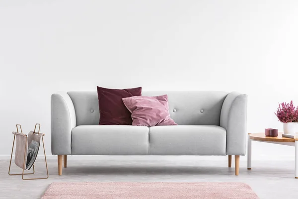 Almofadas lilás e borgonhas no sofá cinza na sala de estar brilhante com urze na mesa de café e espaço de cópia na parede branca vazia — Fotografia de Stock