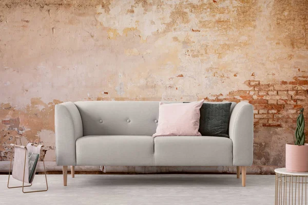 Интерьер гостиной Ваби Саби со старой обветшалой стеной и модным новым диваном с пастельно-розовыми и черными подушками, настоящая фотография — стоковое фото