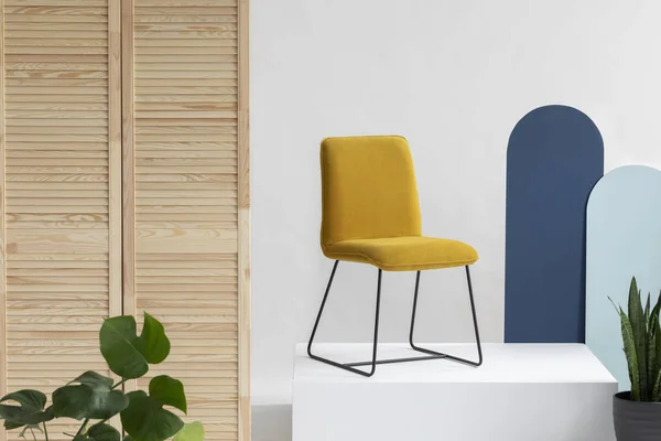 Trendy gele stoel op wit platform in wit en helder interieur met blauwe muur, houten scherm en groene planten — Stockfoto