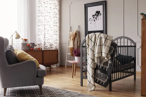 Deken op bed naast leunstoel in de slaapkamer van het grijze baby interieur met poster en raam. Echte foto — Stockfoto