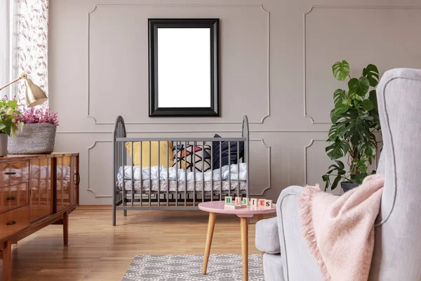 Model van poster boven Cradle in het grijze kind slaapkamer interieur met tafel en fauteuil. Echte foto — Stockfoto