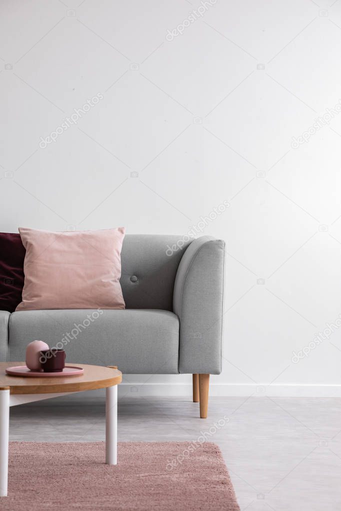 Wooden table on pink carpet in front of grey settee with pillows in white flat interior. Real photo