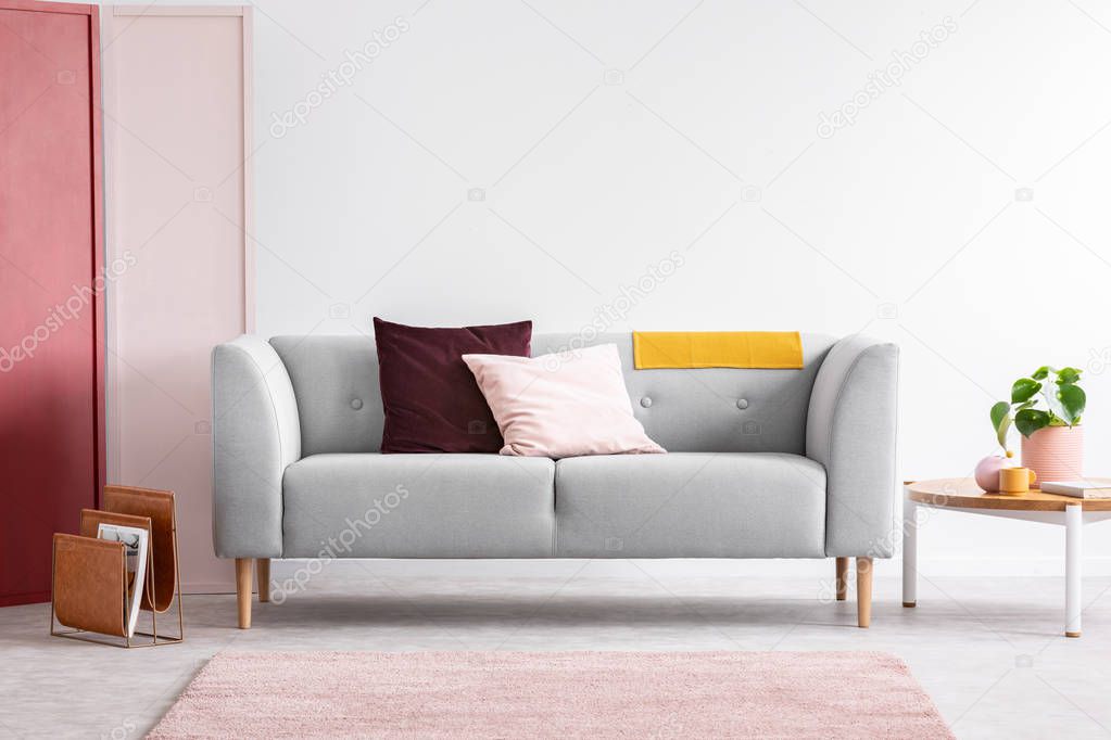 Pastel pink and burgundy pillows on grey sofa in elegant scandinavian living room with red, pink and white wall with copy space