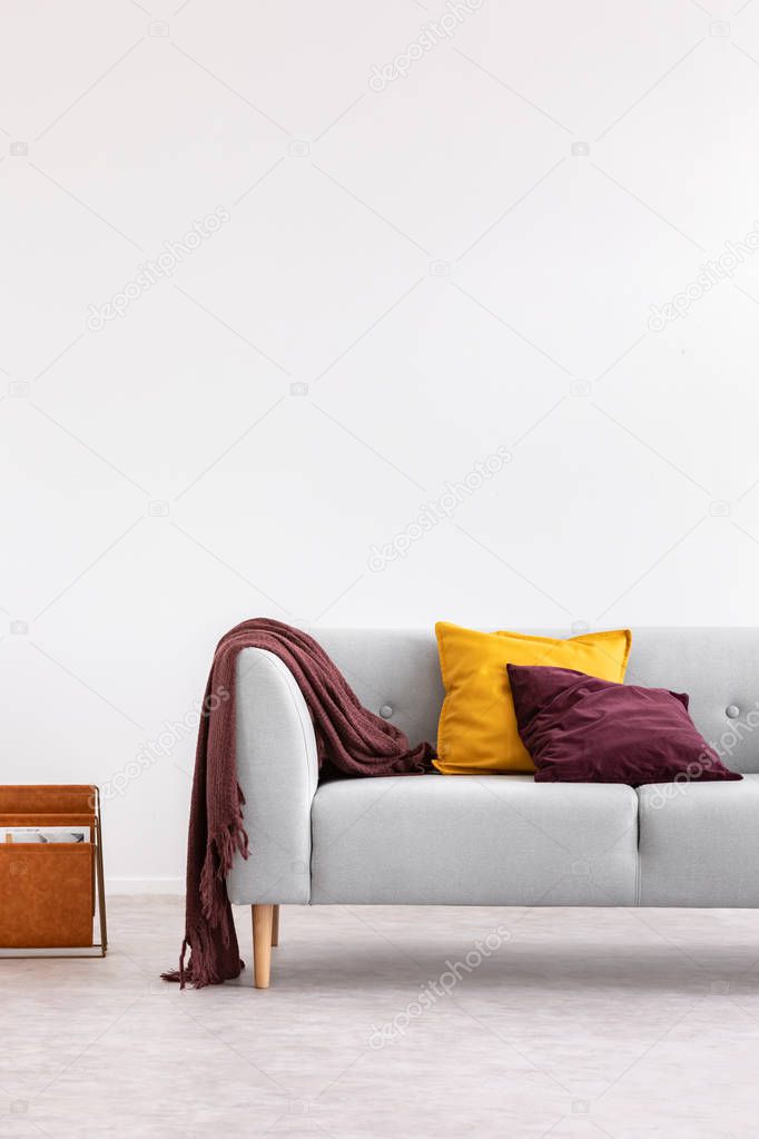 Grey couch with cushions in white minimal living room interior with copy space on the wall. Real photo