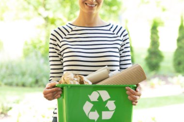 Beautiful smiling woman with green recycling container with paper waste