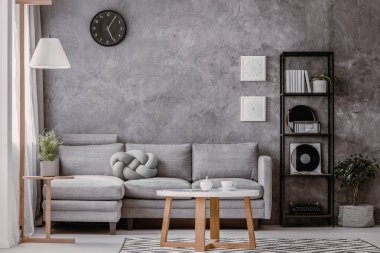 Kopya alanı ve siyah gri beton duvar ile endüstriyel siyah metal bookshelf köşe kanepe pastel gri düğüm yastık ile yanındaki şık oturma odasında saat