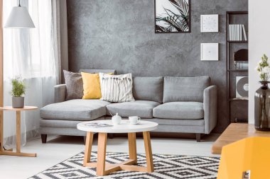 Sehpaya desenli halı gri kanepe yastık ile ile zevkli oturma odasında, boş beton duvar alanı ve Botanik posterinde kopyalama