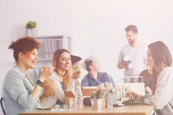 Tre belle amiche sorridenti che mangiano cibo vegetariano durante la pausa pranzo alla corporation — Foto Stock