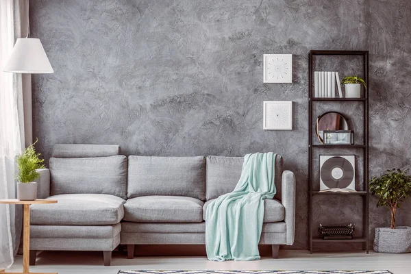 Coperta verde menta su comodo divano grigio in soggiorno contemporaneo con libreria industriale nera, spazio copia su muro di cemento vuoto — Foto Stock