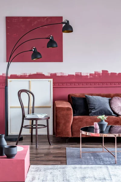 Промышленная модная лампа рядом со стулом с журналами рядом с коричневым угловым диваном с подушками в белом и бордовом интерьере — стоковое фото