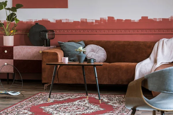 Tavolino con tazze e fiori in vaso davanti al divano marrone in velluto con cuscini in un elegante soggiorno interno — Foto Stock