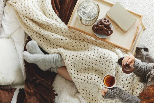 High angle on woman drinking hot tea while sitting on bed with blanket and tray — Stock Photo, Image
