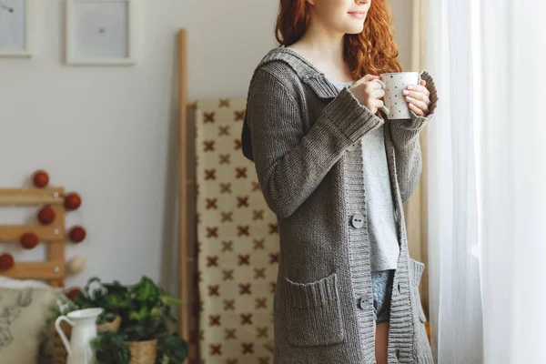 Женщина в свитере и пить чай в спальне интерьер в течение зимы — стоковое фото