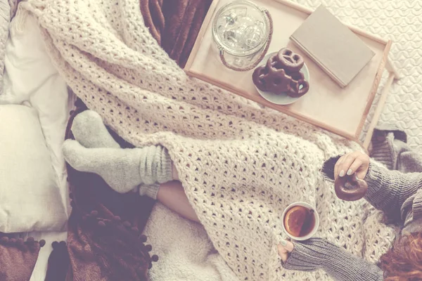Angle élevé sur la personne buvant du thé assis sur le lit avec une couverture et un plateau en bois — Photo