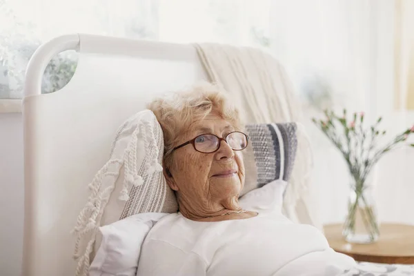 Enfermera mujer mayor con gafas acostada en la cama del hospital —  Fotos de Stock