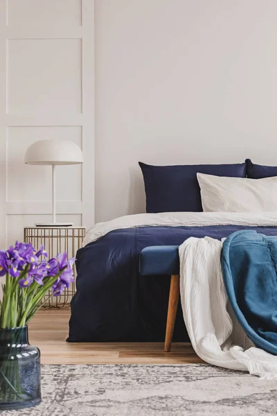 Lâmpada branca na elegante mesa de cabeceira dourada ao lado da cama king size com roupa de cama azul marinho — Fotografia de Stock