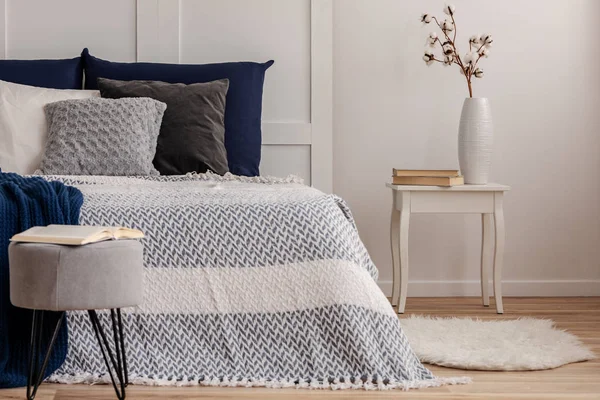 Bloemen in vaas op stijlvolle nachtkastje tafel naast comfortabel bed met witte en blauwe beddengoed — Stockfoto