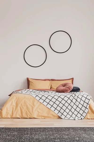 Вертикальный вид на элегантный интерьер спальни с двуспальной кроватью с желтыми и имбирными подстилками и круглыми стенами на пустой белой стене — стоковое фото