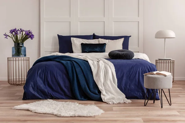 Purple flowers in glass vase and lamp on stylish nightstands on both sides of cozy bed — Stock Image Purple flowers in glass vase and lamp on stylish nightstands on both sides of cozy bed Stock Picture