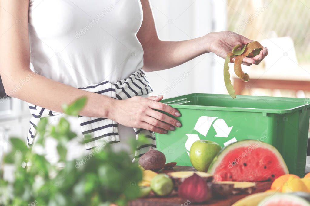 Closeup of eco friendly woman in the kitchen disposing of leftovers of kiwi into compost bin while preparing fruit salad