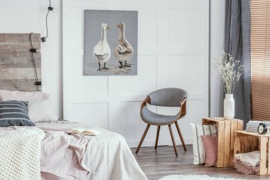 Şık gri sandalye, yastık ve battaniye ve açık kitap ile kral boy yatak ile ahşap kutular ile keyifli yatak odası iç