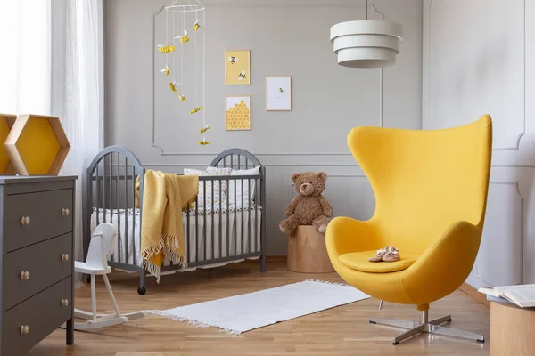 Modne żółte krzesło jajeczne w eleganckiej szarej szkółce z drewnianym łóżeczku i plakatami na ścianie — Zdjęcie stockowe
