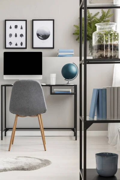 Metallregal mit Büchern und Pflanzen im modernen Home Office mit grauem Stuhl am Industrietisch mit Computer, Poster an grauer Wand — Stockfoto