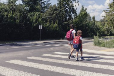 Okula yaya geçidiyle yürüyen sırt çantaları olan çocuklar